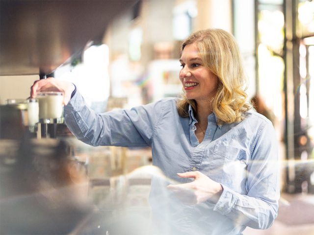 Smiling woman shopping, holding up a candle. Background is light and out of focus.