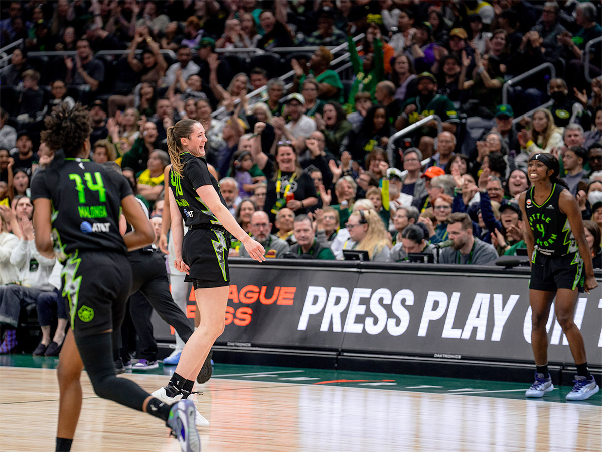 Basketball players celebrating a play on court during a game; crowd is behind them. Credit: Seattle Storm.
